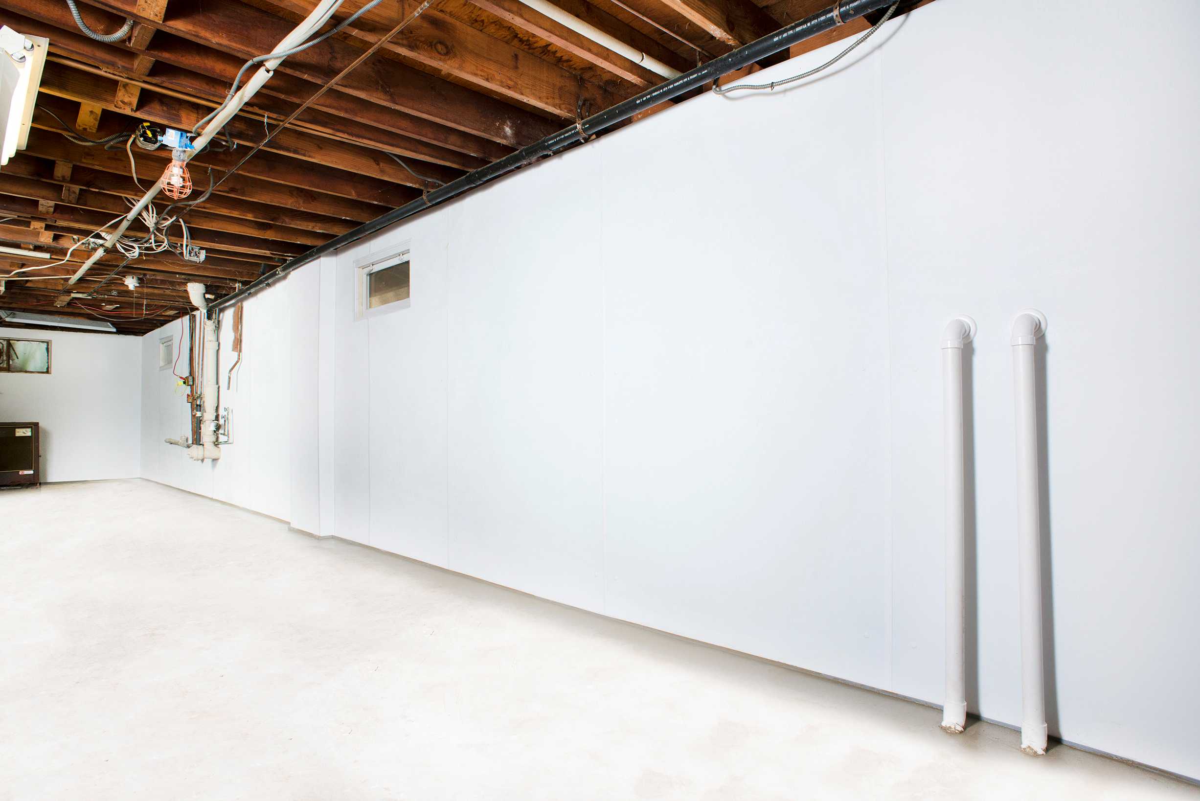After: the same basement wall sealed behind bright waterproof wall paneling by APS, with discharge lines routed to the slab