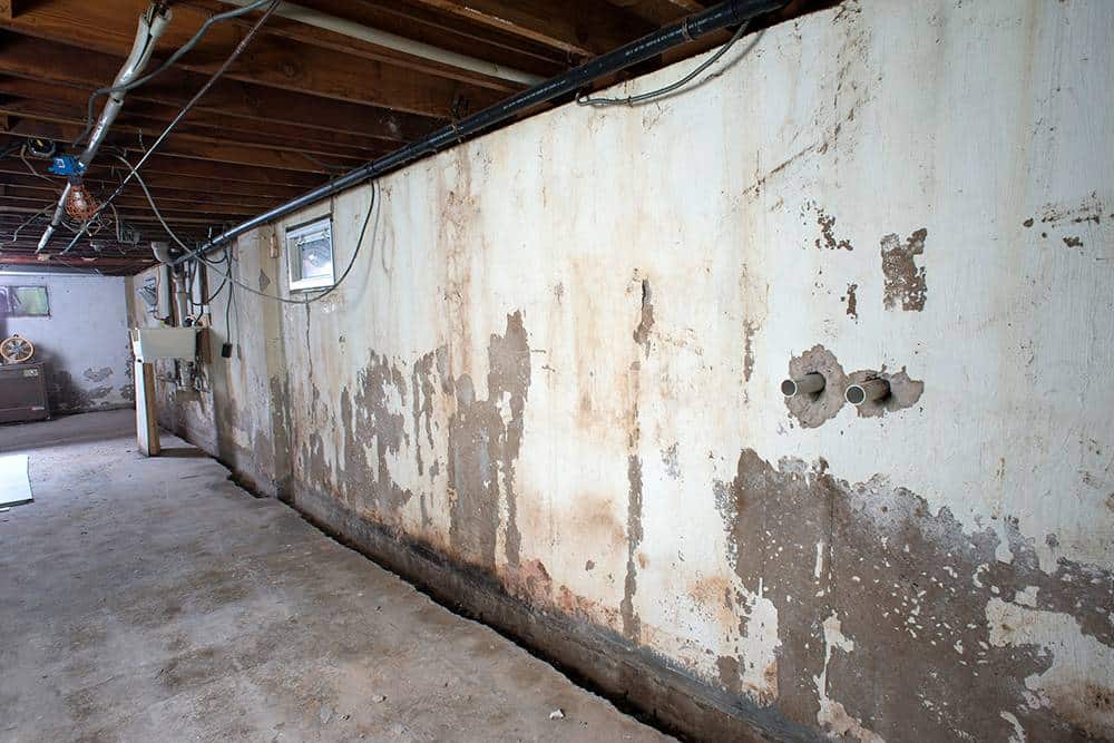 Before: basement block wall with heavy water staining, peeling paint, and efflorescence above a bare slab