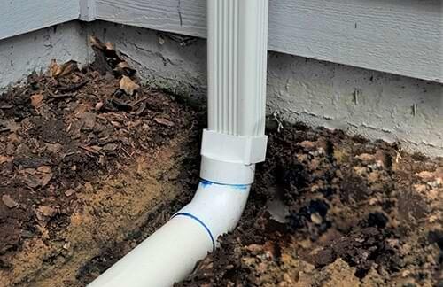 APS Foundation Repair and Waterproofing installing a downspout extension into underground drainage.