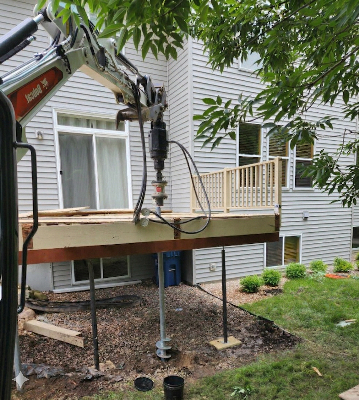 APS Foundation Repair and Waterproofing installing helical deck piers with an excavator to stabilize a residential deck.