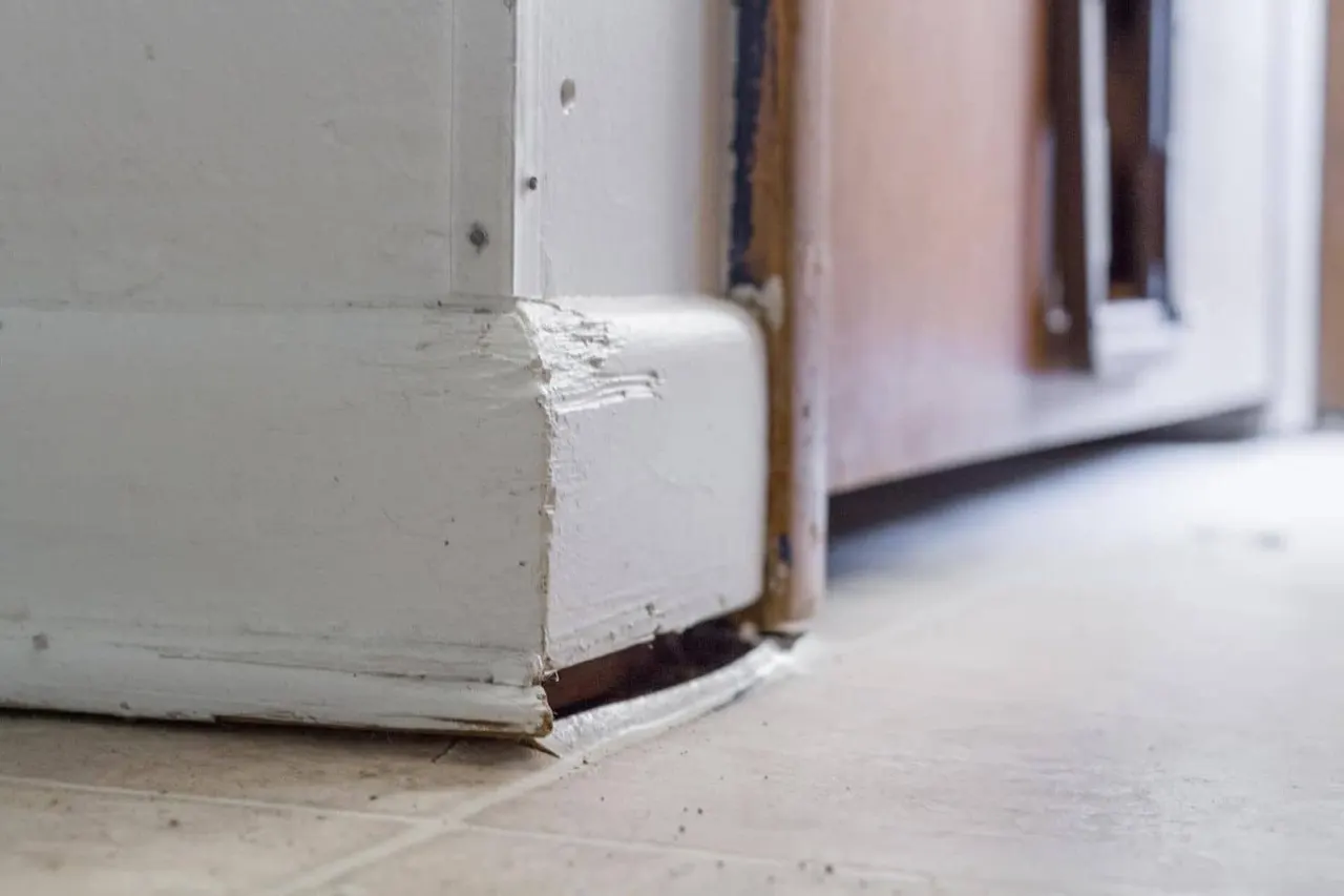 APS Foundation Repair and Waterproofing inspecting uneven floors and a baseboard gap.