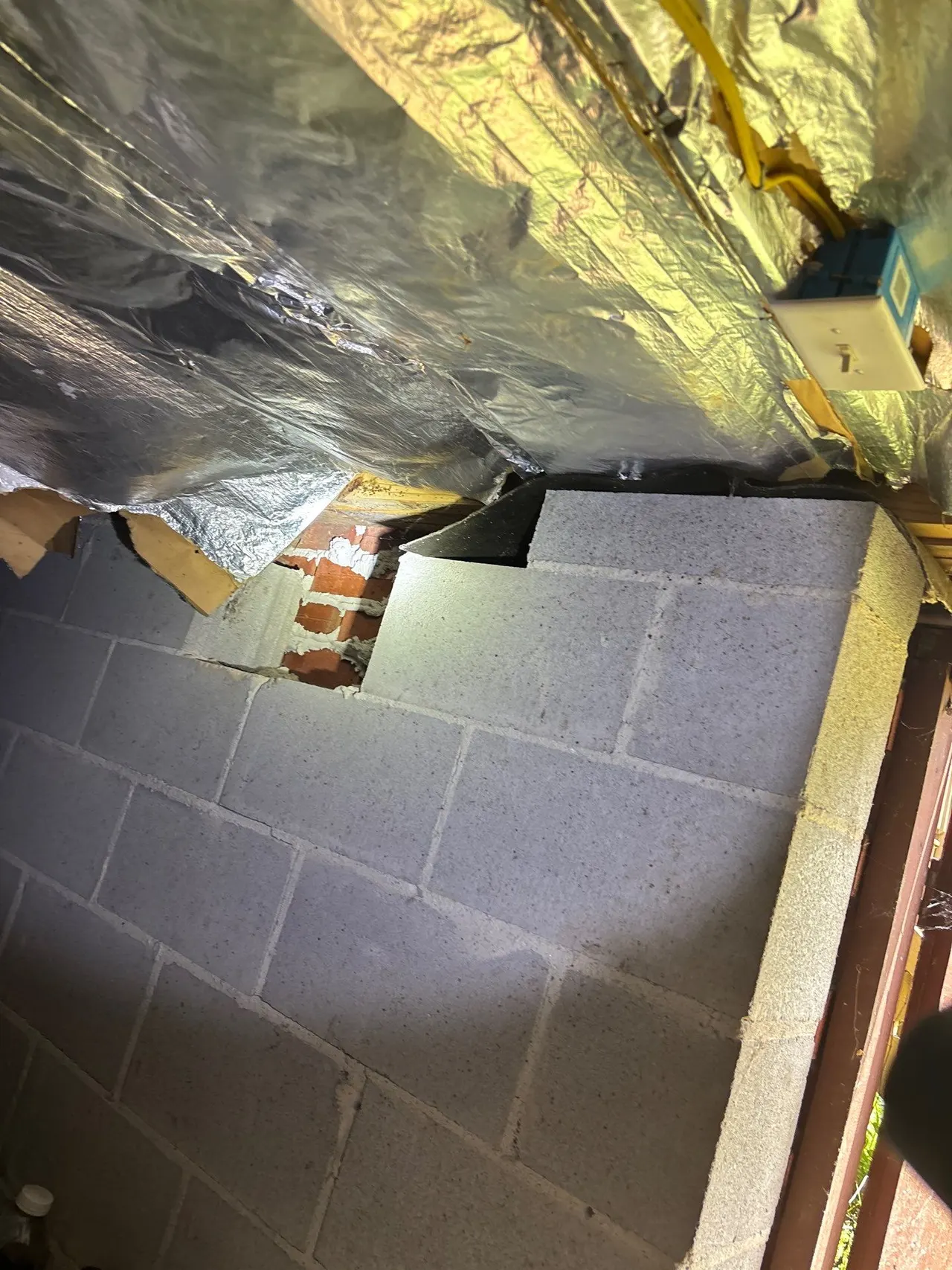 APS Foundation Repair and Waterproofing inspecting a cracked concrete block foundation with exposed brick and stair-step