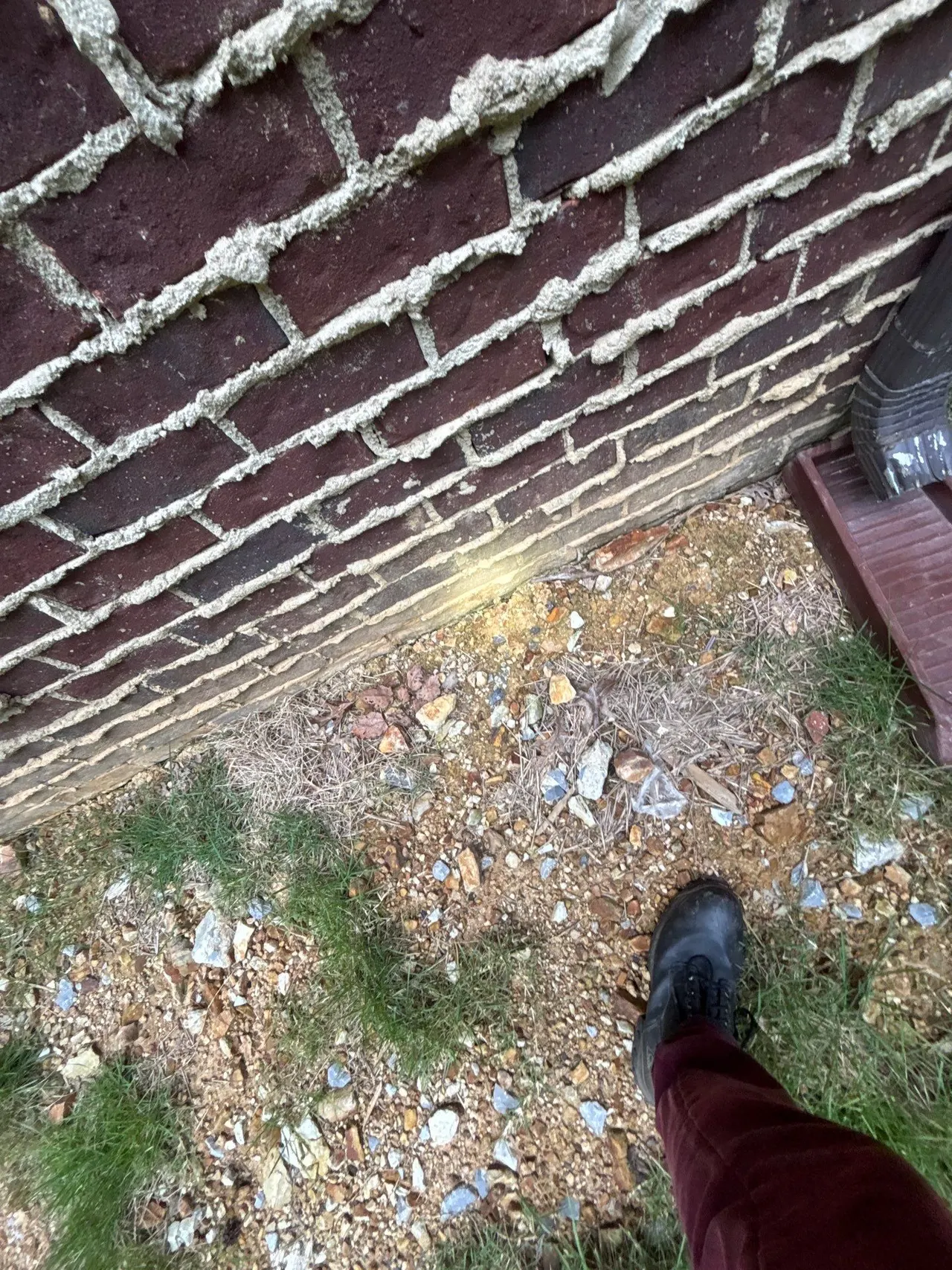 APS Foundation Repair and Waterproofing inspecting exterior foundation wall stains near a downspout in Sterrett, AL