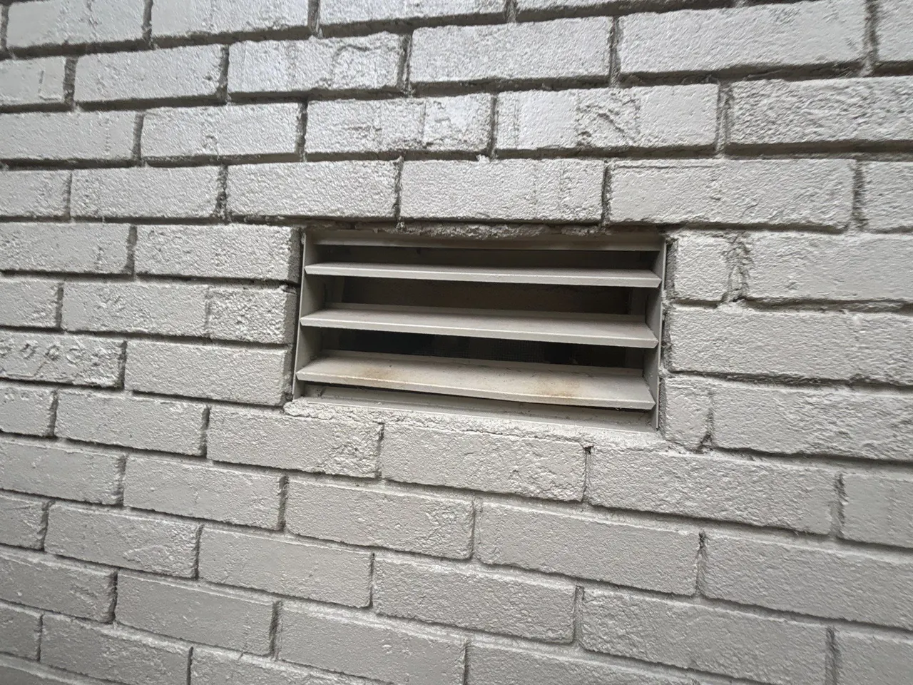 APS Foundation Repair and Waterproofing inspecting an exterior crawl space vent with discoloration on a gray brick