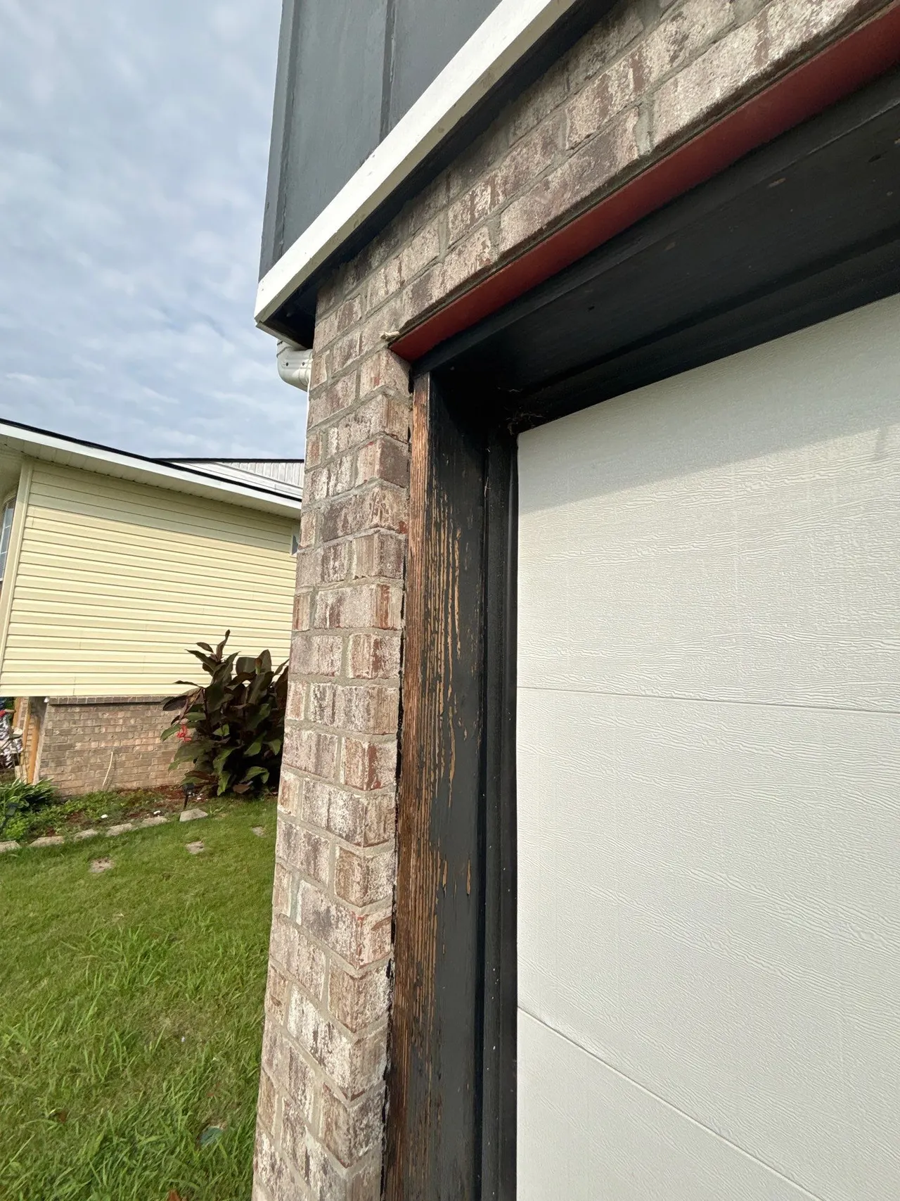 APS Foundation Repair and Waterproofing inspecting cracked bricks and wood damage around a garage door frame in Birmingham