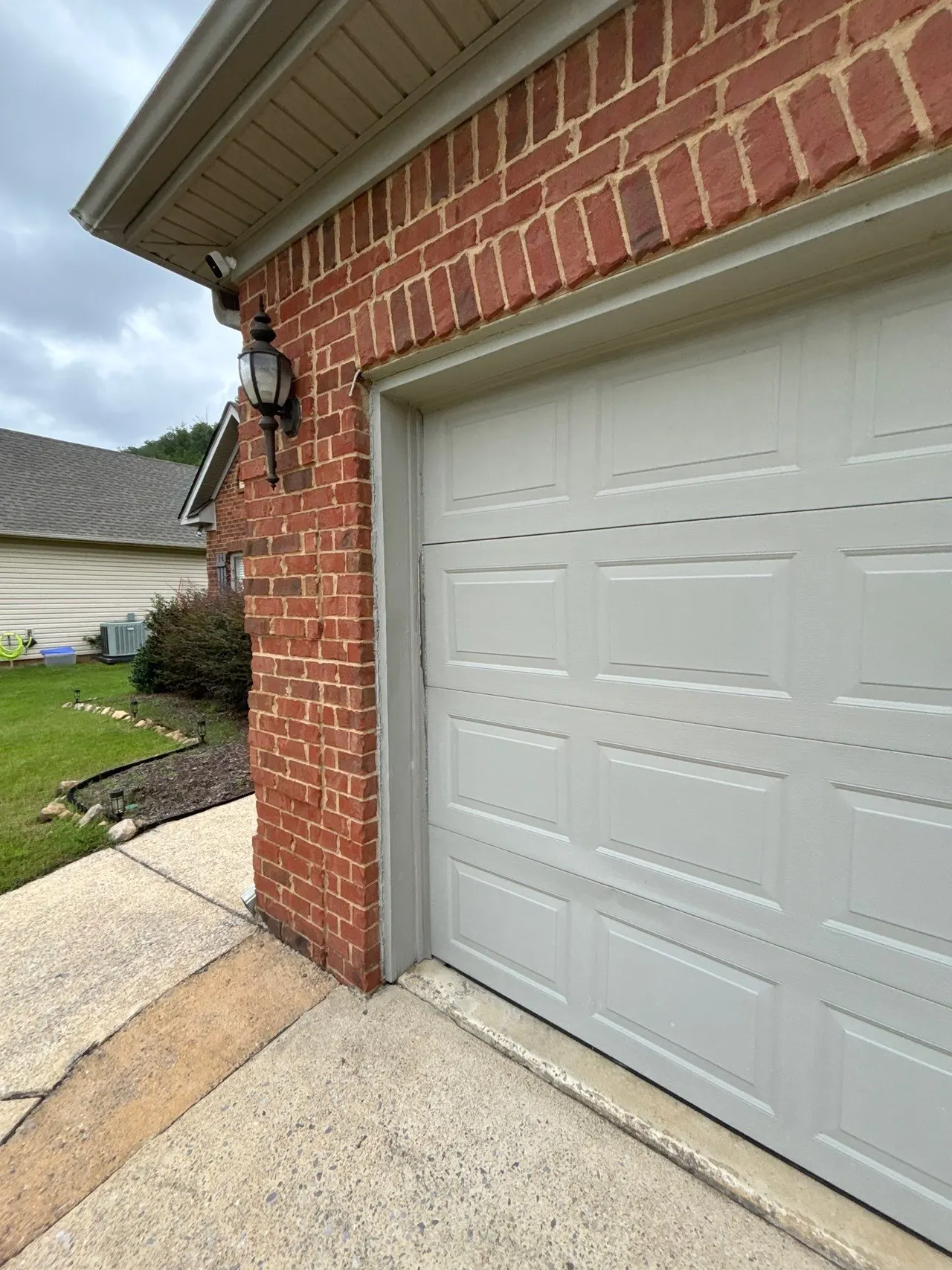 APS Foundation Repair and Waterproofing inspecting a vertical crack in brick siding next to a garage door in Sterrett, AL.