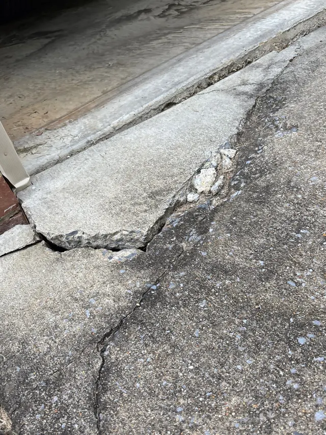 APS Foundation Repair and Waterproofing inspecting a deeply cracked and sunken concrete driveway in Wilsonville, AL.