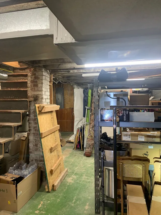 APS Foundation Repair and Waterproofing inspecting an unfinished basement with exposed ceiling joists and stored items