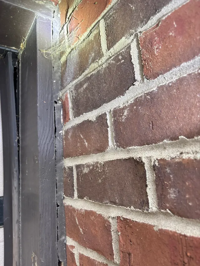 APS Foundation Repair and Waterproofing inspecting a vertical crack in a brick wall next to a wooden door frame in Westover