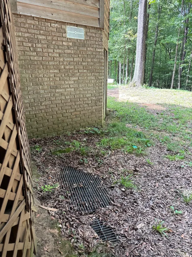 APS Foundation Repair and Waterproofing inspecting a debris-filled drainage grate next to a brick foundation wall