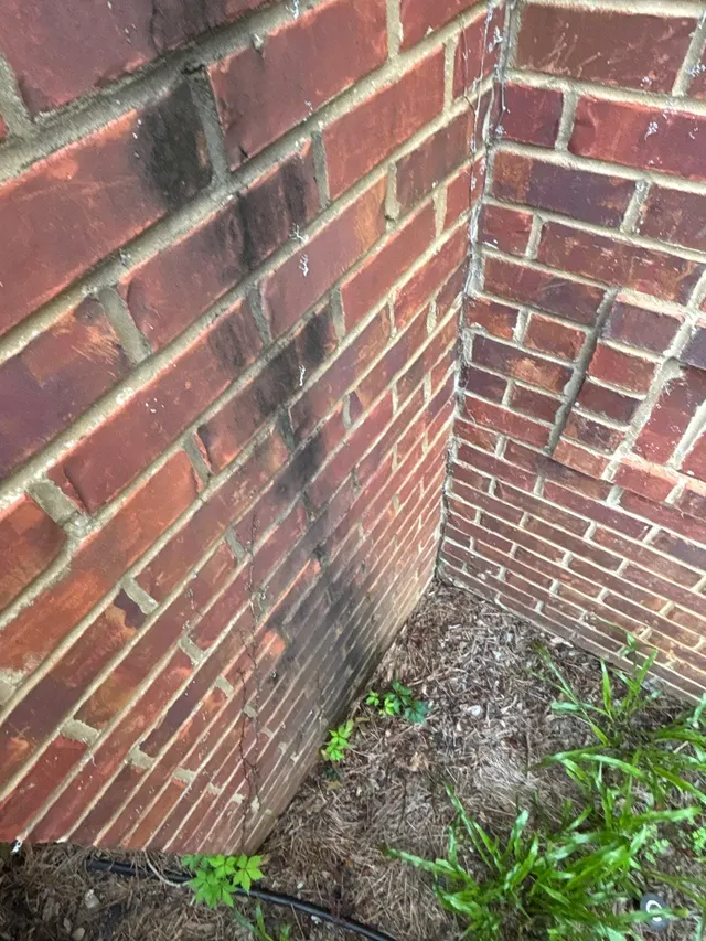 APS Foundation Repair and Waterproofing inspecting vertical cracks in brick house foundation with moisture stains
