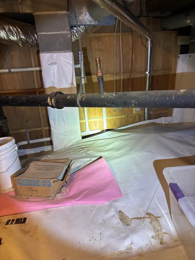 APS Foundation Repair and Waterproofing inspecting a damaged vapor barrier with standing water and debris in a crawl space